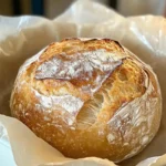 A freshly baked round loaf of artisan bread with a golden, crispy crust and a dusting of flour on top