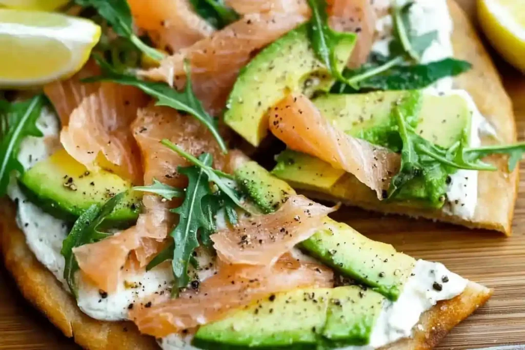 Is breakfast pizza good for you? The Shocking Truth! A close-up of smoked salmon and avocado flatbread topped with arugula and cracked black pepper, served on a wooden board with lemon wedges.