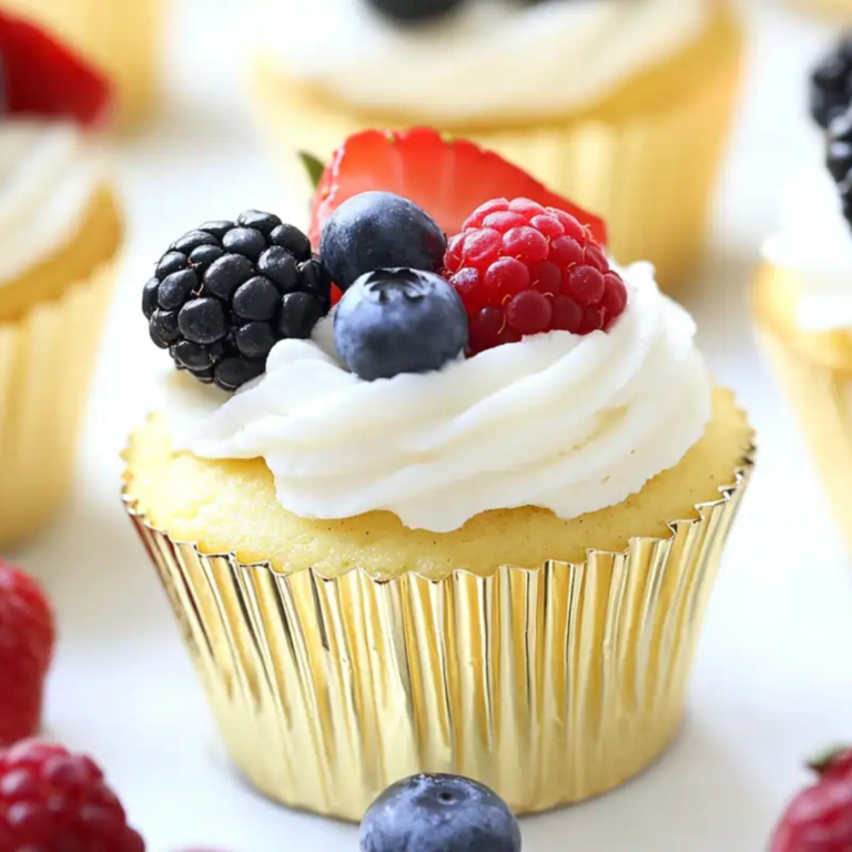 Mini cheesecake cupcakes in gold liners, topped with whipped cream and fresh blackberries, blueberries, raspberries, and strawberries.