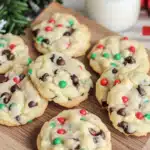 Freshly baked Cake Mix Chocolate Chip Christmas Cookies with red, green, and white sprinkles on a wooden board near a glass of milk.