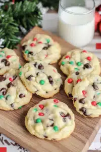 Freshly baked Cake Mix Chocolate Chip Christmas Cookies with red, green, and white sprinkles on a wooden board near a glass of milk.