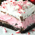 Close-up of a festive no-bake Christmas lasagna dessert slice with layers of chocolate crust, pink filling, and candy cane topping.